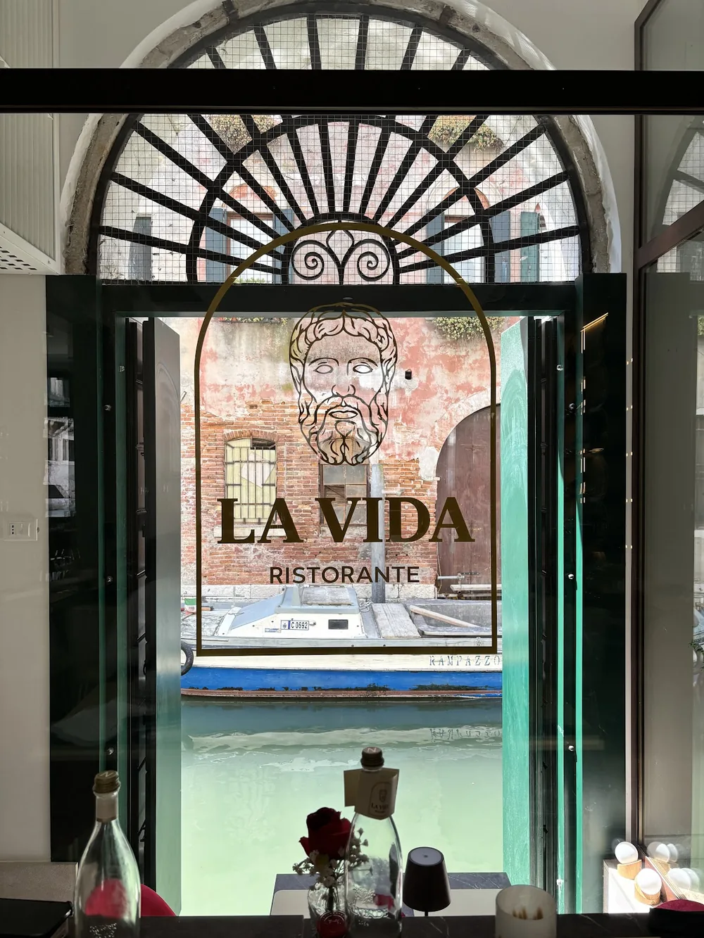 L'insegna di La Vida sulla vetrata ad arco, con il canale e le case di fronte.