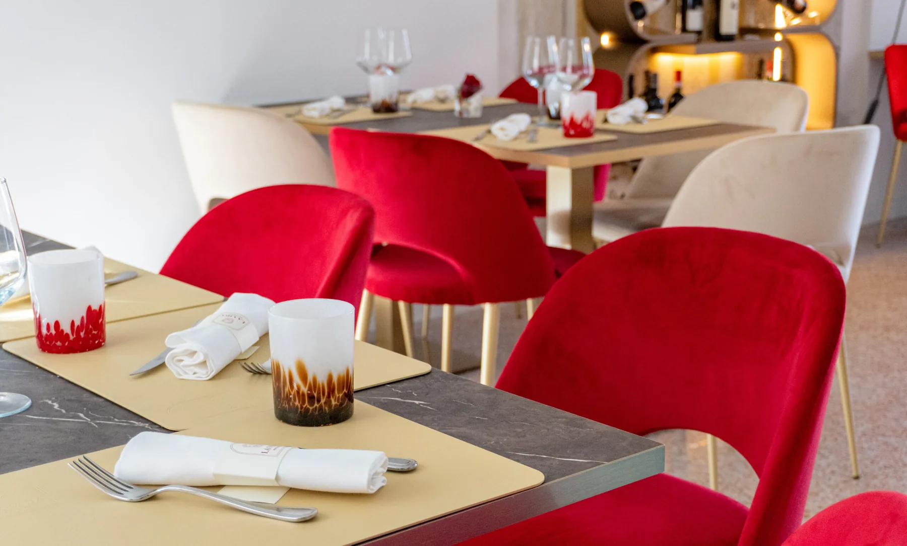 Tavoli in marmo scuro con sedie in velluto rosso nella sala dalle pareti bianche.